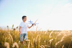The kid runs with a toy plane. Son dreams of flying. Happy child, boy, runs on the sun playing with a toy airplane on the summer field photo