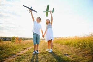 Running boy and girl holding two green and blue airplanes toy in the field during summer sunny day photo