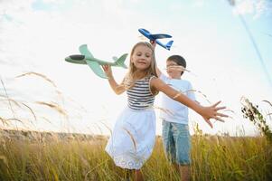 Running boy and girl holding two green and blue airplanes toy in the field during summer sunny day photo