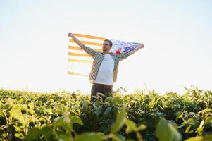A young farmer stands with a USA flag in a soybean field. The concept of the US agricultural industry. photo
