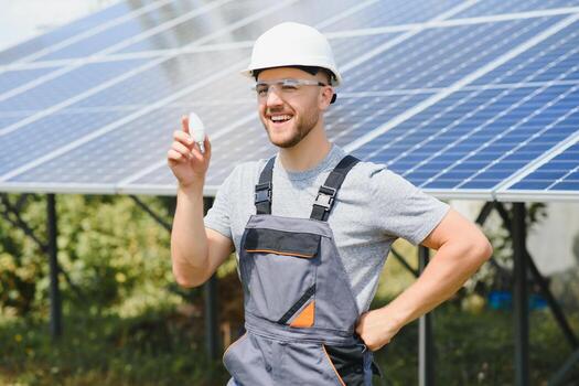 Technical expert in solar photovoltaic panels, remote control performs routine actions to monitor the system using clean renewable energy in the hand a light bulb. photo