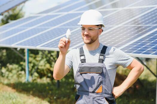 Technical expert in solar photovoltaic panels, remote control performs routine actions to monitor the system using clean renewable energy in the hand a light bulb. photo