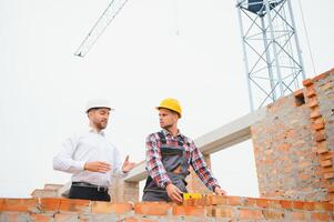 Construction engineers supervising progress of construction project stand on new concrete floor top roof and crane background. photo