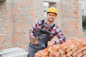 Construction worker man in work clothes and a construction helmet. Portrait of positive male builder in hardhat working at construction site. photo