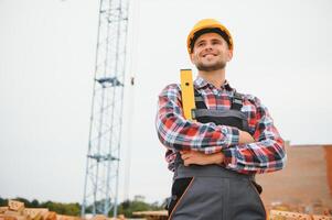Using bricks. Young construction worker in uniform is busy at the unfinished building photo