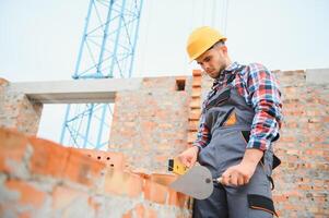 Using bricks. Young construction worker in uniform is busy at the unfinished building photo