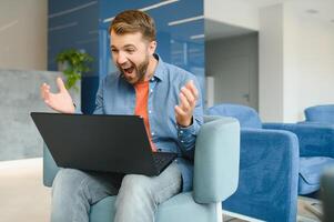 happy smiling remote online working man in casual outfit with laptop in joyful successful winning gesture sitting in an coworking office at a work desk. photo
