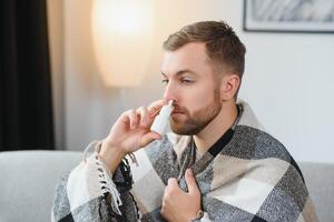 Sick man with nasal spray and paper tissue at home photo