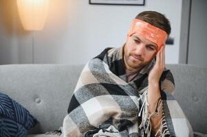 A sick man sits at home on a gray sofa with a blanket. Illness, protection, coronavirus, illness, flu photo