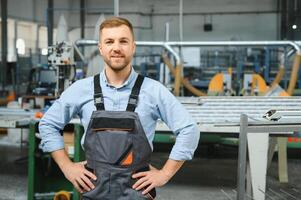 Portrait of factory worker in protective uniform and hardhat standing by industrial machine at production line. People working in industry photo