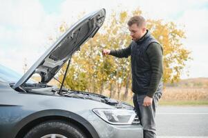 driver trying to figure out how to fix broken down car with red triangle to warn other road users photo