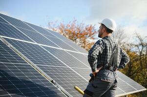 Professional worker installing solar panels on the metal construction, using different equipment, wearing helmet. Innovative solution for energy solving. Use renewable resources. Green energy. photo