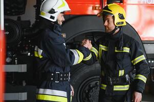 Two firefighters in protective clothing in helmets with fire engine, friendly handshake photo