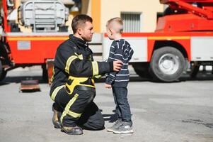 Portrait of rescued little boy with firefighter man standing near fire truck. Firefighter in fire fighting operation. photo