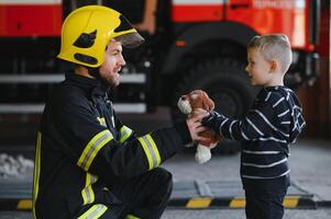 A firefighter take a little child boy to save him. Fire engine car on background. Fireman with kid in his arms. Protection concept. photo