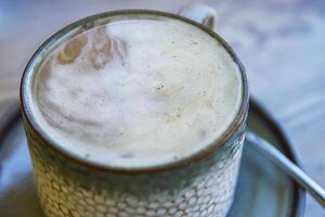 Top view of white cream foam slowly dissolving in the black coffee rotating and mixing in the ceramic mug on the plate with spoon. Latte or macchiato creamy texture. Breakfast. Top view. Close up. photo