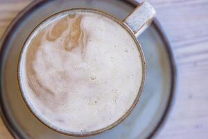 Top view of white cream foam slowly dissolving in the black coffee rotating and mixing in the ceramic mug on the plate with spoon. Latte or macchiato creamy texture. Breakfast. Top view. Close up. photo
