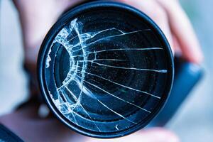 Hands of young photographer holding DSLR photo camera with broken lens filter glass after if fall down onto the floor. Close up. Destroyed cracked photo-filter. Macro. Top view. Selective focus.