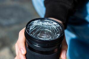 Hands of young photographer holding DSLR photo camera with broken lens filter glass after if fall down onto the floor. Close up. Destroyed cracked photo-filter. Macro. Top view. Selective focus.