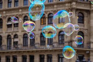 Many multicolored giant soap bubbles flying in the air on a windy day. Huge bubble are stretching on the wind into long smoothy changing form without popping. Close up. Copy space. Selective focus. photo