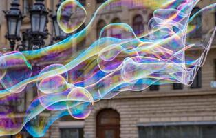 Many multicolored giant soap bubbles flying in the air on a windy day. Huge bubble are stretching on the wind into long smoothy changing form without popping. Close up. Copy space. Selective focus. photo