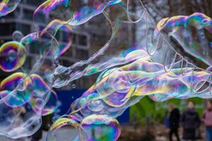 Many multicolored giant soap bubbles flying in the air on a windy day. Huge bubble are stretching on the wind into long smoothy changing form without popping. Close up. Copy space. Selective focus. photo