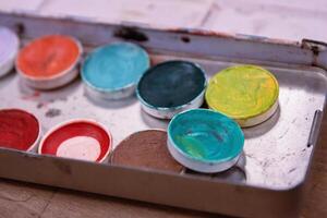 Closeup of an Used colorful make up palette with a lot of eye shadows. Green, blue, navy, yellow, orange, sparkly blue. Grease paint. Stage makeup workshop banner. Selective focus. photo
