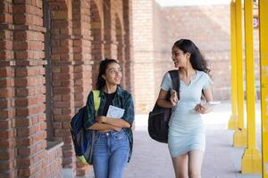 Two Close Friends Are Looking At Each Other While Carrying Bags On Their Shoulders and Holding Books photo