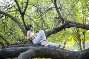 Young Lady is Lying On a Tree Branch and Using Her Smartphone photo