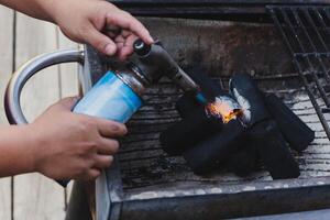 Man using BBQ lighter torch to start fire for charcoal. photo