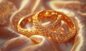 Pair of intricately designed gold bracelets arranged on a smooth satin material background photo
