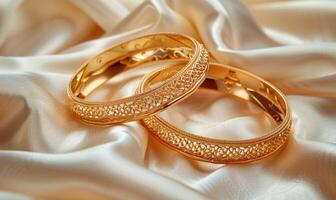 Pair of intricately designed gold bracelets arranged on a smooth satin material background photo