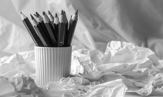 Graphite pencils arranged in a cup on a desk, surrounded by crumpled sheets of discarded white paper photo