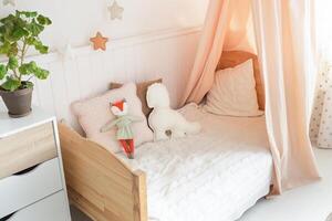 A cozy and bright children's bed with a canopy has cute soft toys on the bed. There is a green plant next to the bed. light background photo