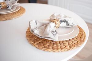 close-up of a white table set in boho style with a wicker stand and linen napkin.kitchen table photo