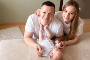 parents play with a baby at home on a bed covered with a linen bedspread. family concept. happy parenthood concept. happy parents look into the frame hugging the baby photo