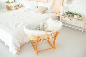 large bright bedroom with white walls and a large bed with a white knitted bedspread. near the bed there is a small wicker cradle with a toy. family expecting pregnancy photo