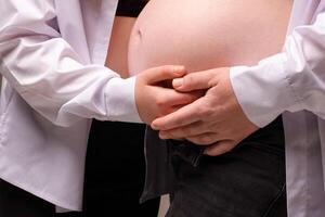 close-up photograph of a pregnant belly being hugged by the hands of mother and baby. family expecting a baby photo