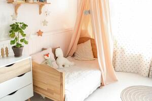 A cozy and bright children's bed with a canopy has cute soft toys on the bed. Next to the bed there is a green plant on the chest of drawers. light background photo