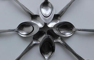 Silvery table and dessert spoons laid out in a flower shape isolated on white surface photo