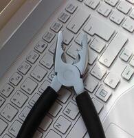 PC Support Concept Image. Metal Pliers On Laptop Keypad Closeup View photo