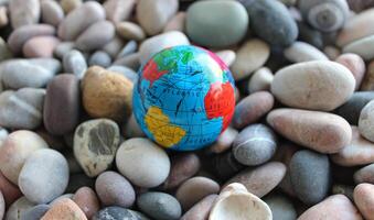 Miniature globe on a sea stones with conventionally drawn continents, oceans and trade routes on it photo