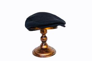 Concept photo of a classic flat cap or scally cap made of warm wool. Classic black hat mounted on bronze mannequin head on white studio background