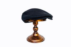 Concept photo of a classic flat cap or scally cap made of warm wool. Classic black hat mounted on bronze mannequin head on white studio background