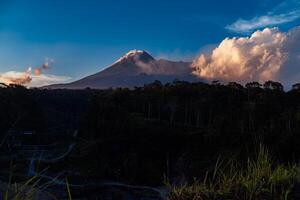 Panorama of Mount Merapi at dusk is very clear with the blue sky and green forest in the foreground with a ravine where cold lava flows. The landscape of Mount Merapi is truly enchanting and charming photo