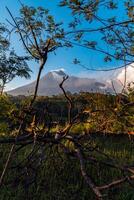 Panorama of Mount Merapi at dusk is very clear with the blue sky and green forest in the foreground with a ravine where cold lava flows. The landscape of Mount Merapi is truly enchanting and charming photo
