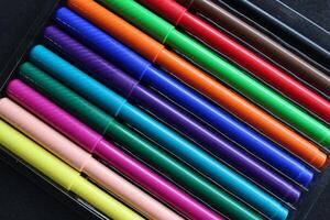 A set of twelve colored felt-tip pens in a transparent box on a black background photo