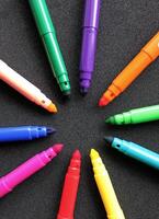Open felt tip pens of different colors in the shape of a star lie on a black background vertical photo
