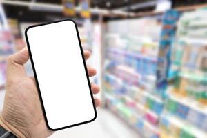 Hand holding blank screen smartphone for copy space on blurred Miscellaneous Product shelf. e-commerce app shopping mockup. social media, payment and shopping online concept. photo