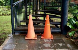 Two orange triangle traffic cone barrier as a do not climb or enter sign isolated on horizontal ratio outdoor park environment and black metal staircase objects. photo